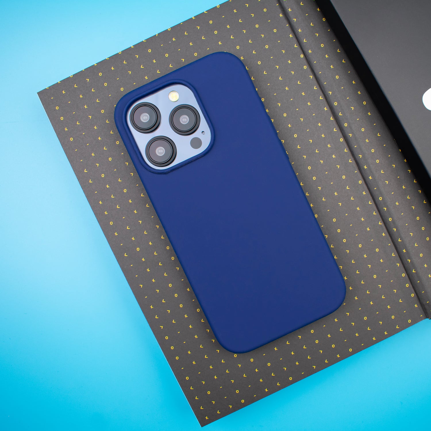 The Slim Navy Blue SKNS SILICONE Magnetic iPhone 15 Pro Case Resting on an Open Notebook