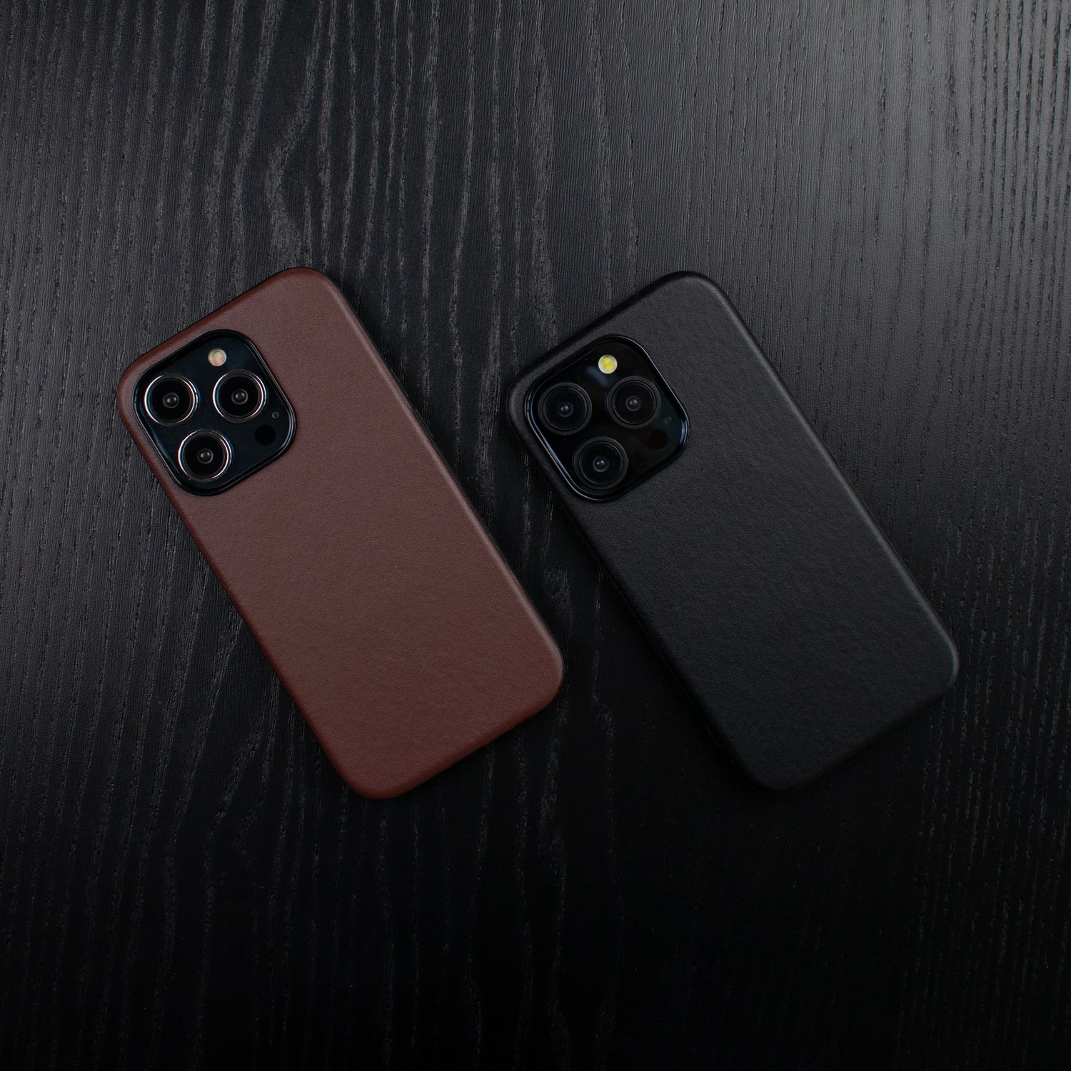 Side by side images of the SKNS LEATHER iPhone 15 Pro Case in brown and black on a dark wood table showing off the premium finish