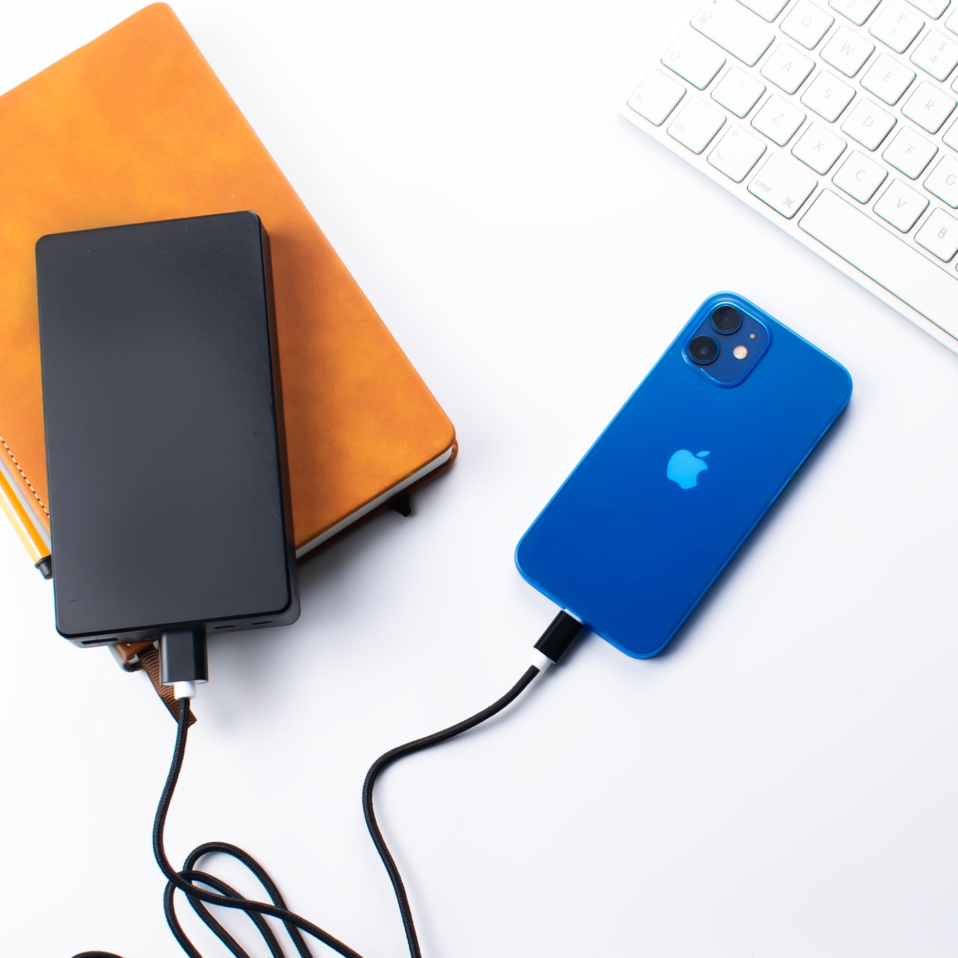 Lifestyle image of the SKNS Nylon braided lightinng cable charging an iphone from a power bank on a office desk